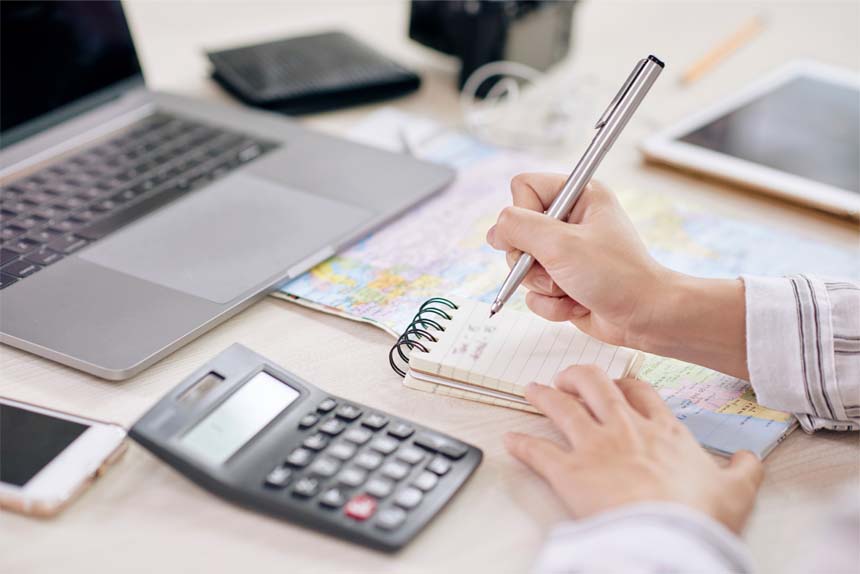 woman taking notes in notepad sitting at desk with laptop and calculator