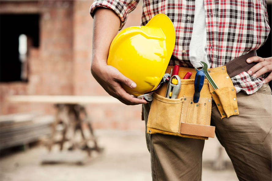 construction worker clutching a yellow hard hat with tools secured around their waist