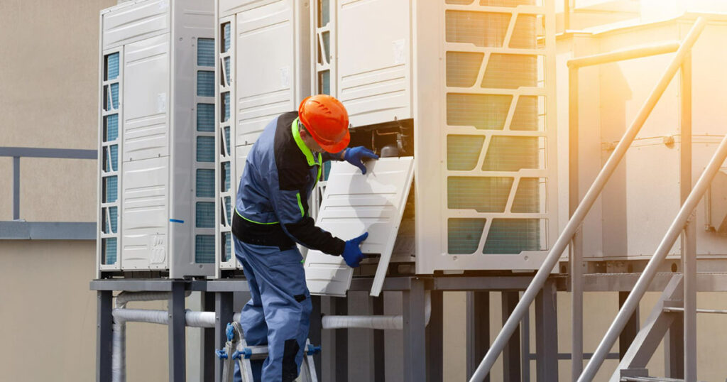 Maintenance personnel conducting repairs on the rear of a large air conditioner