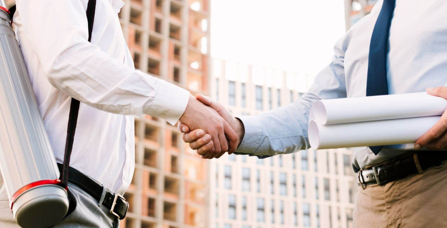 Business individuals wearing white long-sleeved shirts shake hands outdoors.