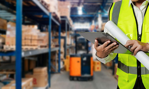 man in the warehouse with a tablet and a rolled-up warehouse plan