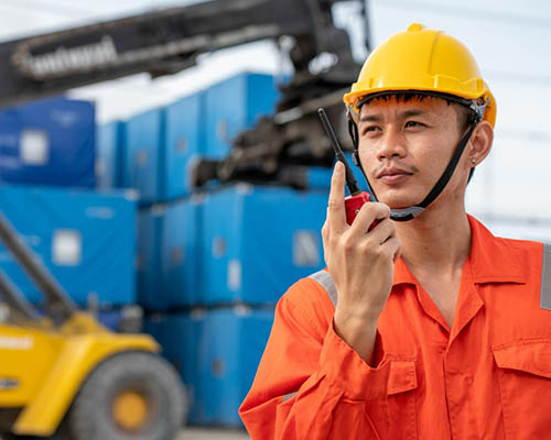 outdoor scene with a worker in a hard hat communicating via a walkie-talkie