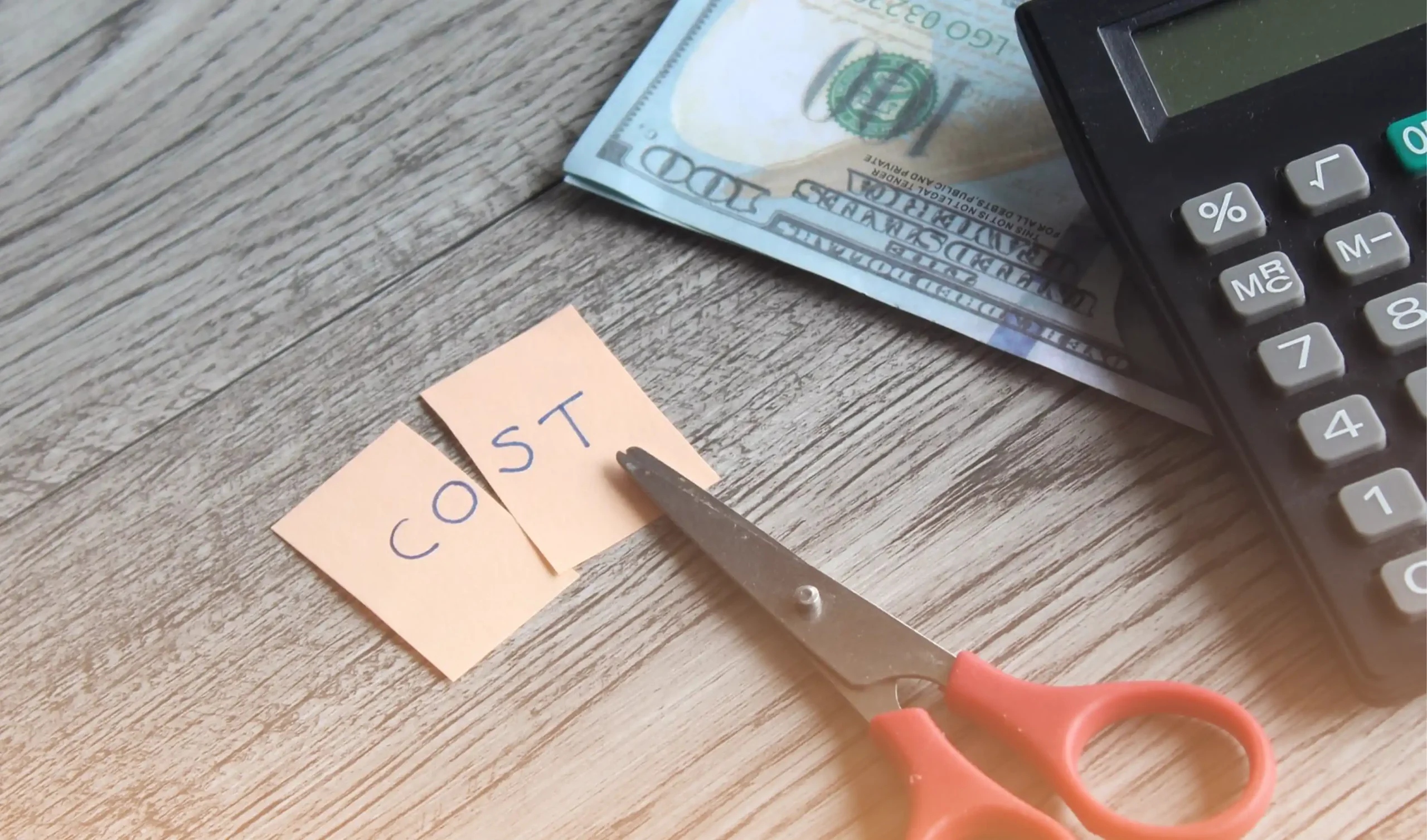 Scissors cutting a paper labeled 'COST,' with cash and a calculator in the background, illustrating labor cost reduction